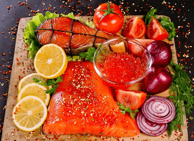 나무 도마 위에 연어구이, 생 연어, 연어알, 빨간 양파, 잘려진 노란 레몬, 상추, 로즈마리가 가득하다. 위에는 고추가루와 후추가루가 잔뜩 뿌려졌다.