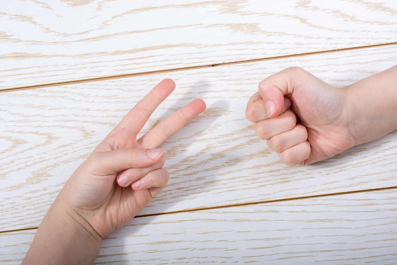hands-making-rock-paper-scissors-gesture-on-wooden-background