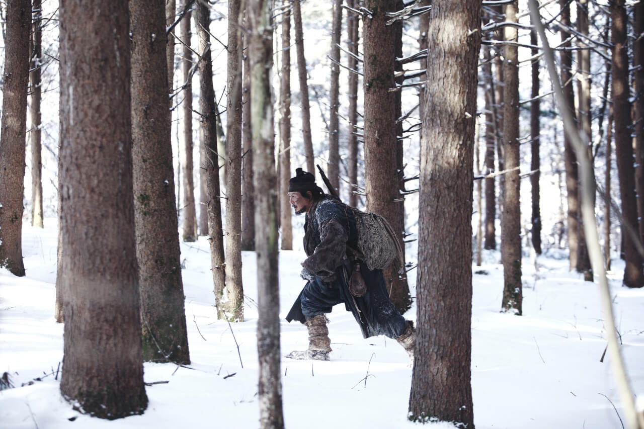 눈 쌓인 숲의 나무 사이를 걷는 남자