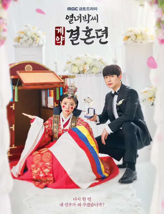 열녀박씨 계약결혼뎐 두 주인공 공식포스터-
흰색 결혼식장 가마 앞 혼례복을 입은 이세영의 난처한 표정과 결혼정장을 입은 배인혁이 결혼반지를 건내는 모습