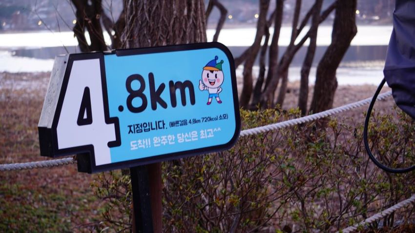 하늘색 바탕 팻말에 써 놓은 4.8km, 뒤로 잡목, 호수물,
