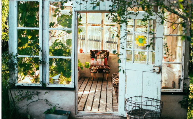 초록 식물과 햇살이 가득한 온실 안, 편안한 의자가 놓인 아늑한 공간. 새로운 출발과 안정된 보금자리를 상징하는 장면