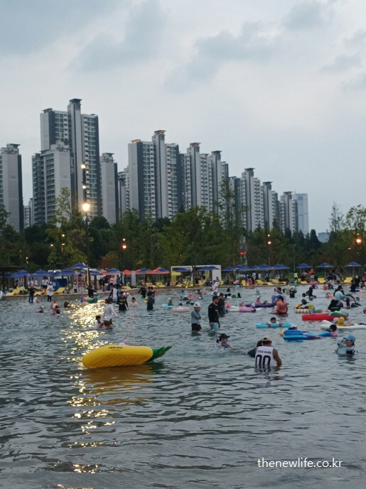 해질 무렵 콘 모양 튜브와 다양한 튜브를 띄운 사람들이 물놀이를 즐기는 잠실 한강공원 물놀이장