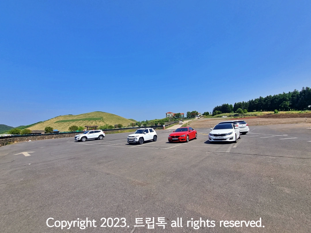 오른쪽 뒤에 새별오름이 보이는 넓은 야외 주차장