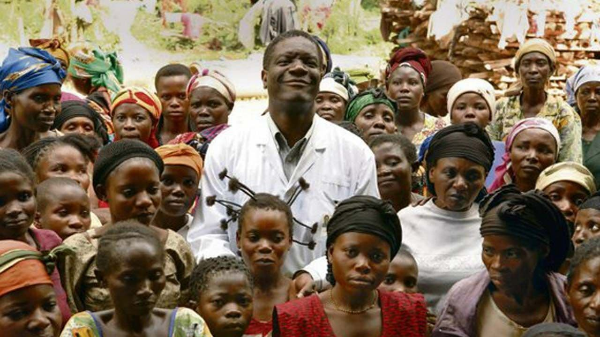 수십 명의 콩고 여성들을 구한 의사 무쿼게가 의사 가운을 입고 한가운데 미소 띤 인자한 얼굴로 서 있고, 콩고 여성들이 그의 주변을 둘러싸고 있는 사진