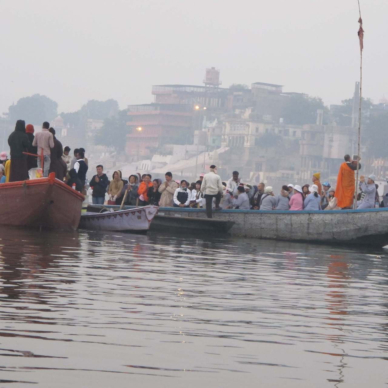 밤이 된 강가에서 화려한 조명 아래 많은 인파가 모여 힌두교 제례 의식인 아르띠 뿌자를 관람하는 장면