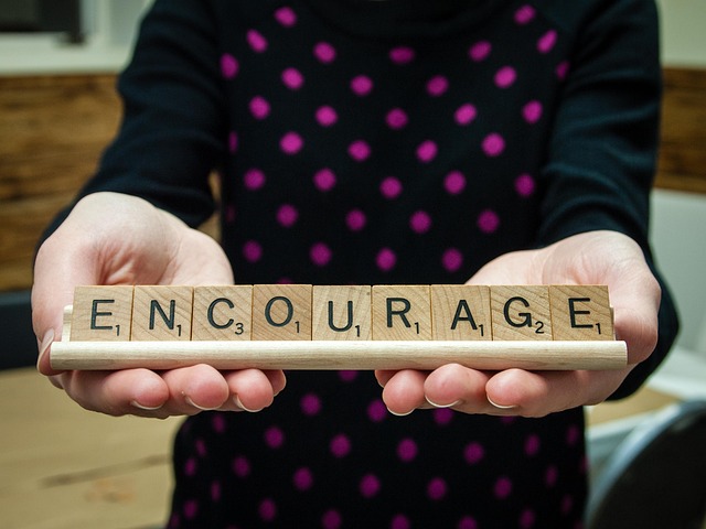 나무 스크래블 조각으로 만든 ENCOURAGE(격려하다) 단어를 손으로 들고 있는 모습, 긍정적 지지와 응원의 중요성을 상징