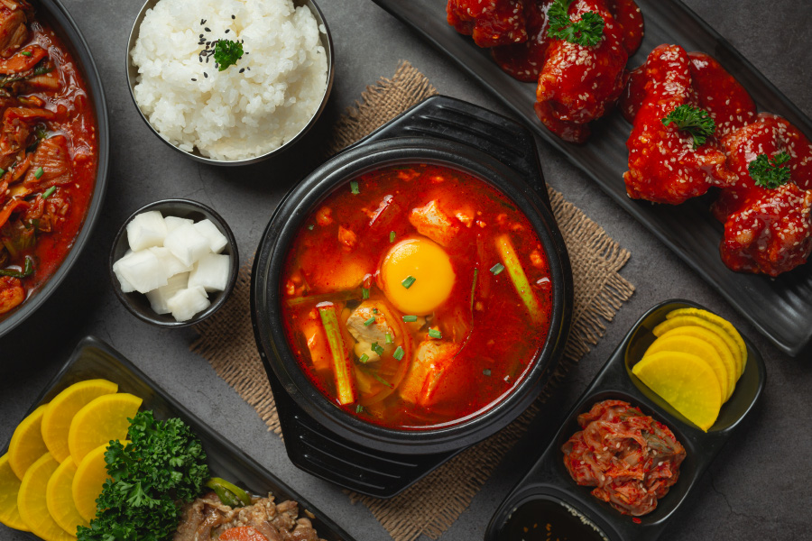 검은 테이블 위에 흰쌀밥을 담은 그릇과 순두부찌개를 담은 뚝배기, 김치찜을 담은 냄비, 단무지와 김치, 무저림, 게장 등을 각각 담은 그릇을 놓아두고 위에서 찍은 사진