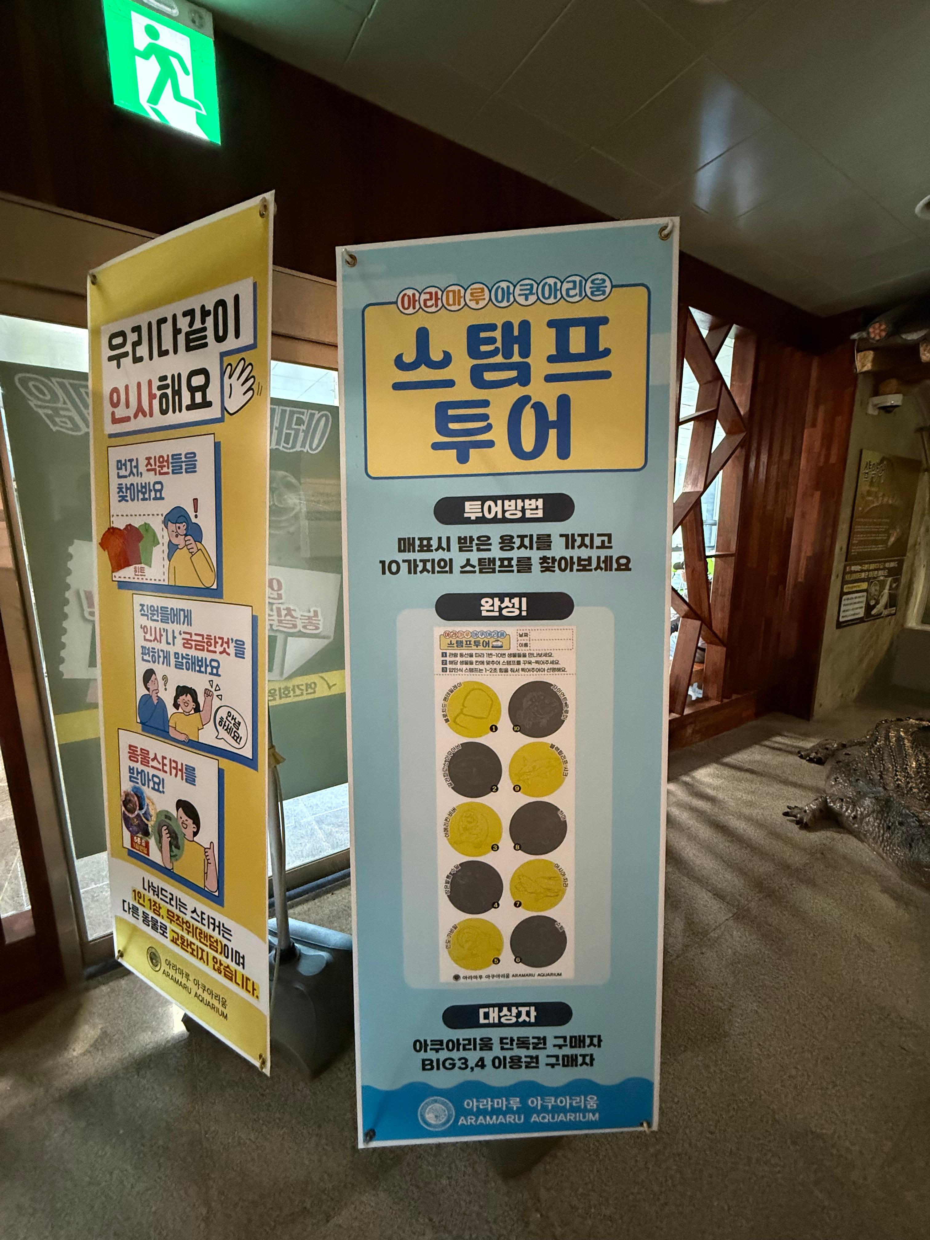 아쿠아리움 내부에 설치된 두 개의 배너. 하나는 직원에게 인사하라는 내용이고, 다른 하나는 10개의 스탬프를 모으는 '스탬프 투어' 프로그램을 안내하고 있습니다.