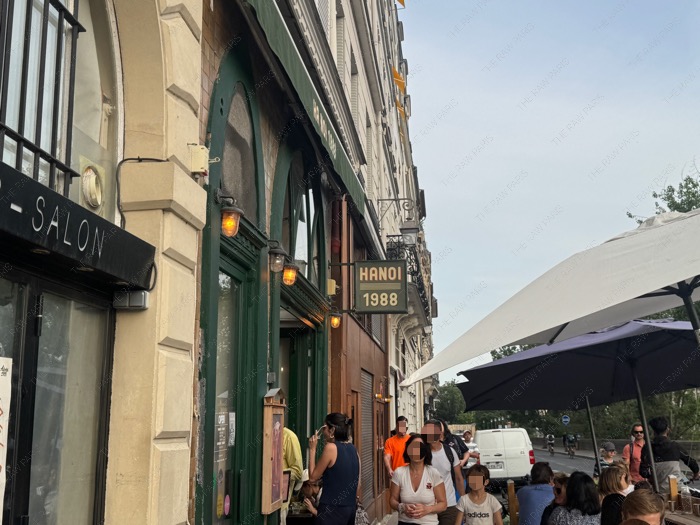 The stylish green storefront of Hanoi 1988 restaurant in Paris with a classic sign and outdoor seating ❘ La devanture verte élégante du restaurant Hanoi 1988 à Paris avec une enseigne classique et des sièges en terrasse