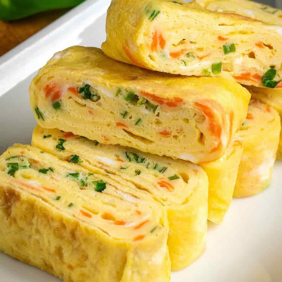 당근과 파가 고르게 섞인 부드러운 계란말이 한 줄이 흰 접시위에 놓인 모습