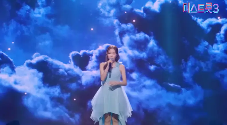 미스트롯3- 파란배경 파란드레스를 입고 오른손으로 마이크를 들고 긴머리를 늘어뜨리며 노래하는 정서주