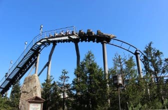 청룡열차에 사람들이 타 있고 레일 밑으로 나무들이 있다