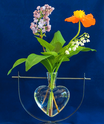 투명한 하트 유리병에 꽃들이 있다. 하얀 은방울꽃, 주황색 커다란 꽃이다.