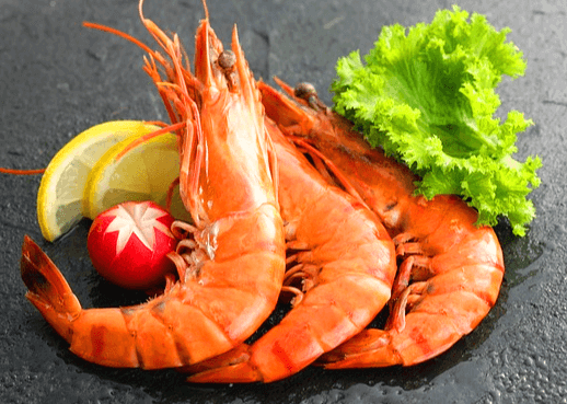 회색 식탁 위에 잘 익은 통새우 3마리가 있다. 상추와 레몬 조각도 있다.