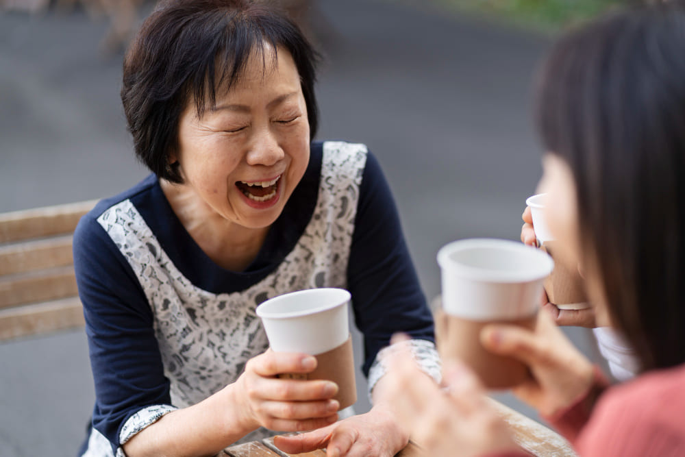 중년 여성 두 명이 커피를 마시며 웃고 있다.