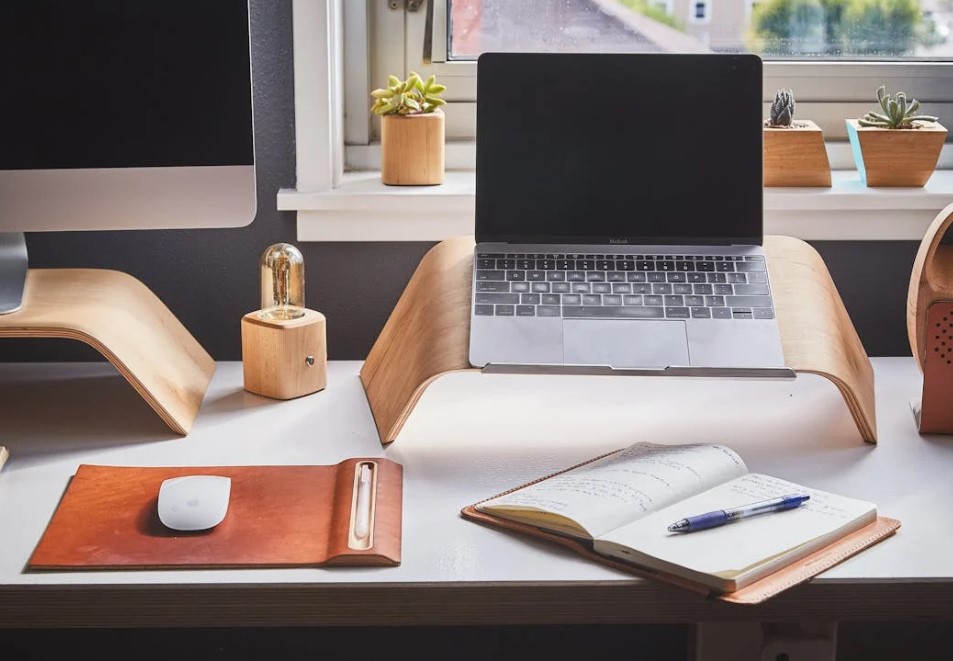 창가 책상 위 노트북과 노트북 받침대, 필기노트가 놓인 작업 공간