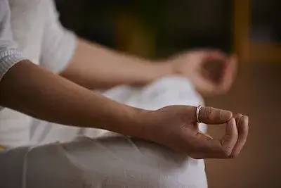 하얀 옷을 입고 두 다리를 교차해 포개고 앉아 두 손을 엄지와 검지를 붙이고 손바닥을 위로 향하게 하여 무릎에 올리고 명상하고 있는 사람.