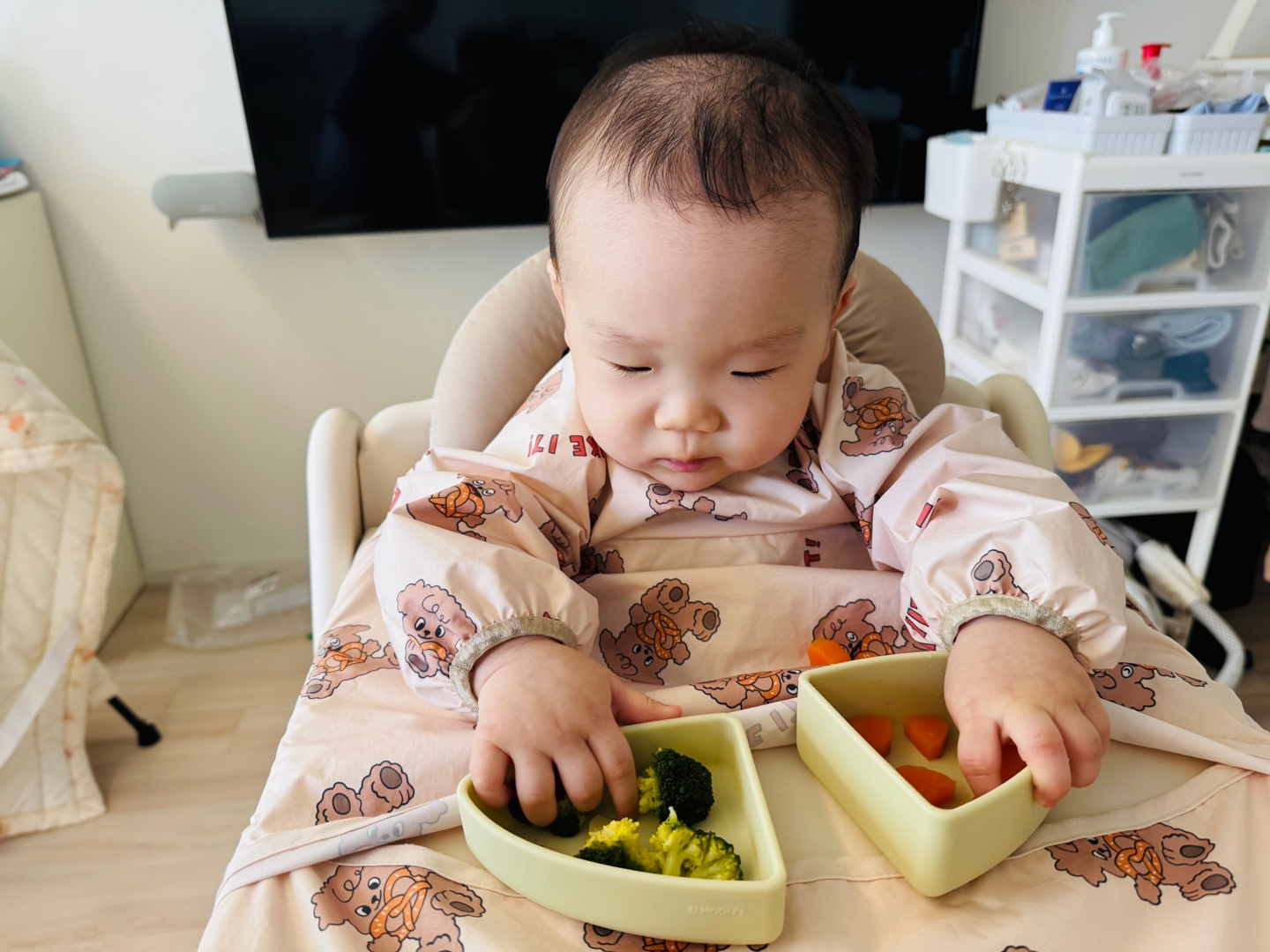 찬솔이가 브로콜리와 당근 스틱을 두 손으로 진지하게 바라보는 점심 식사 장면