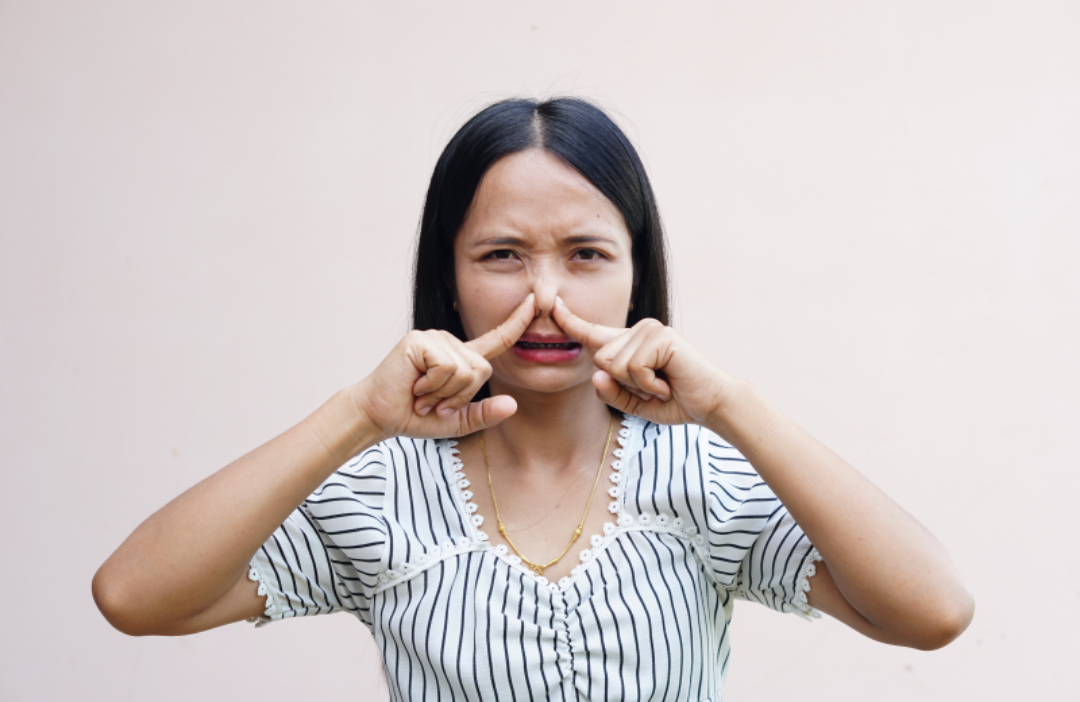 한 여자가 양손으로 코를 막고 있다.