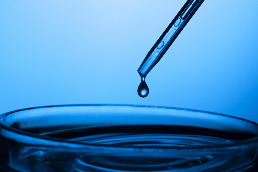 파란색 광을 배경으로 바닥의 물컵으로 스포이드에서 물방울이 한 방울 떨어지는 순간을 찍은 사진