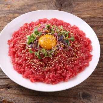 흰-접시에-소고기-육회가-선홍빛을-띠고-새싹야채와-그-위에-노른자가-얹어져-식감을-돋우며-마무리는-깨를-뿌려놓은-육회-한접시
