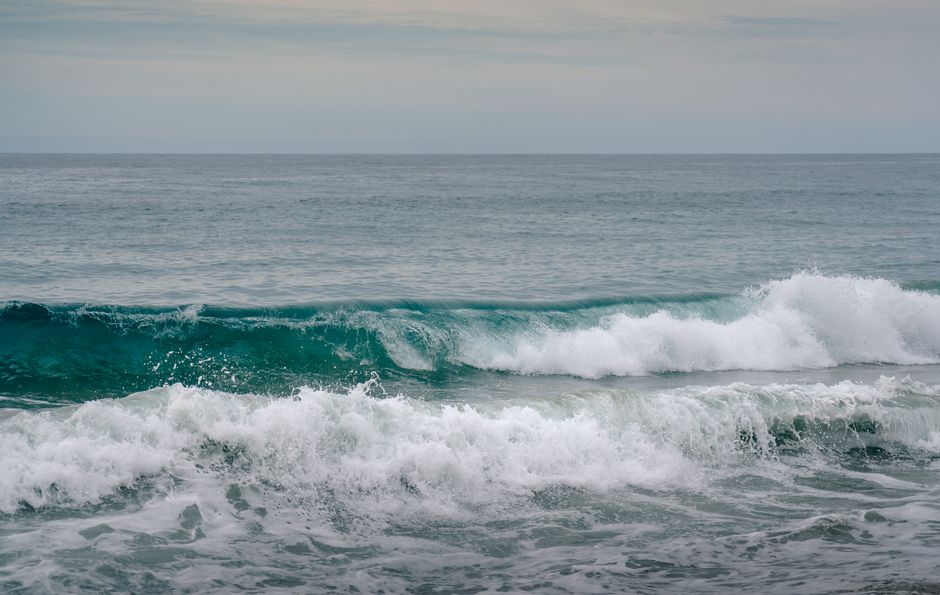 Tranquil view of ocean waves crashing onto the sandy shore under a calm cloudy sky.