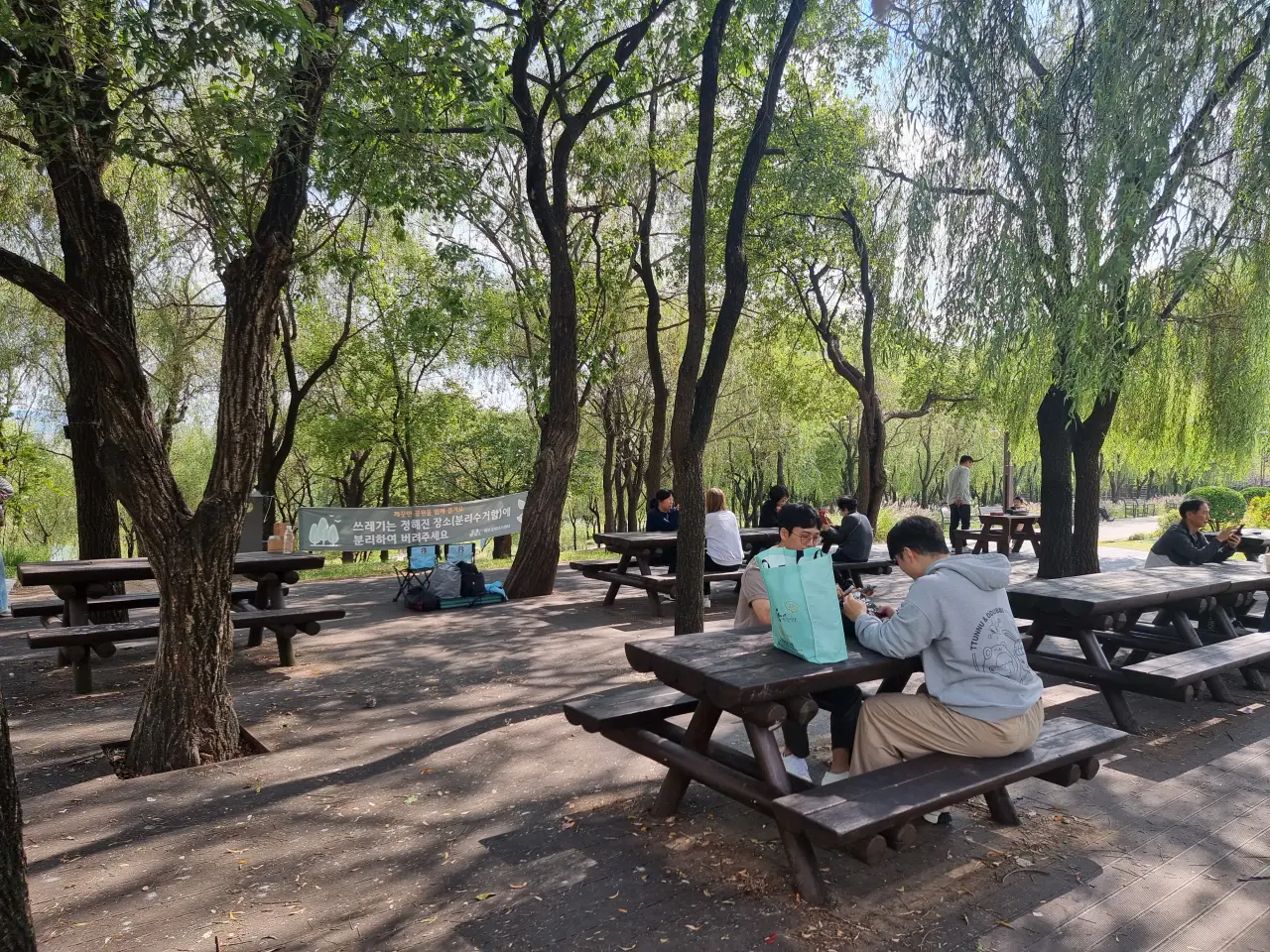 나무-그늘-아래-야외-테이블-앉아있는-사람들