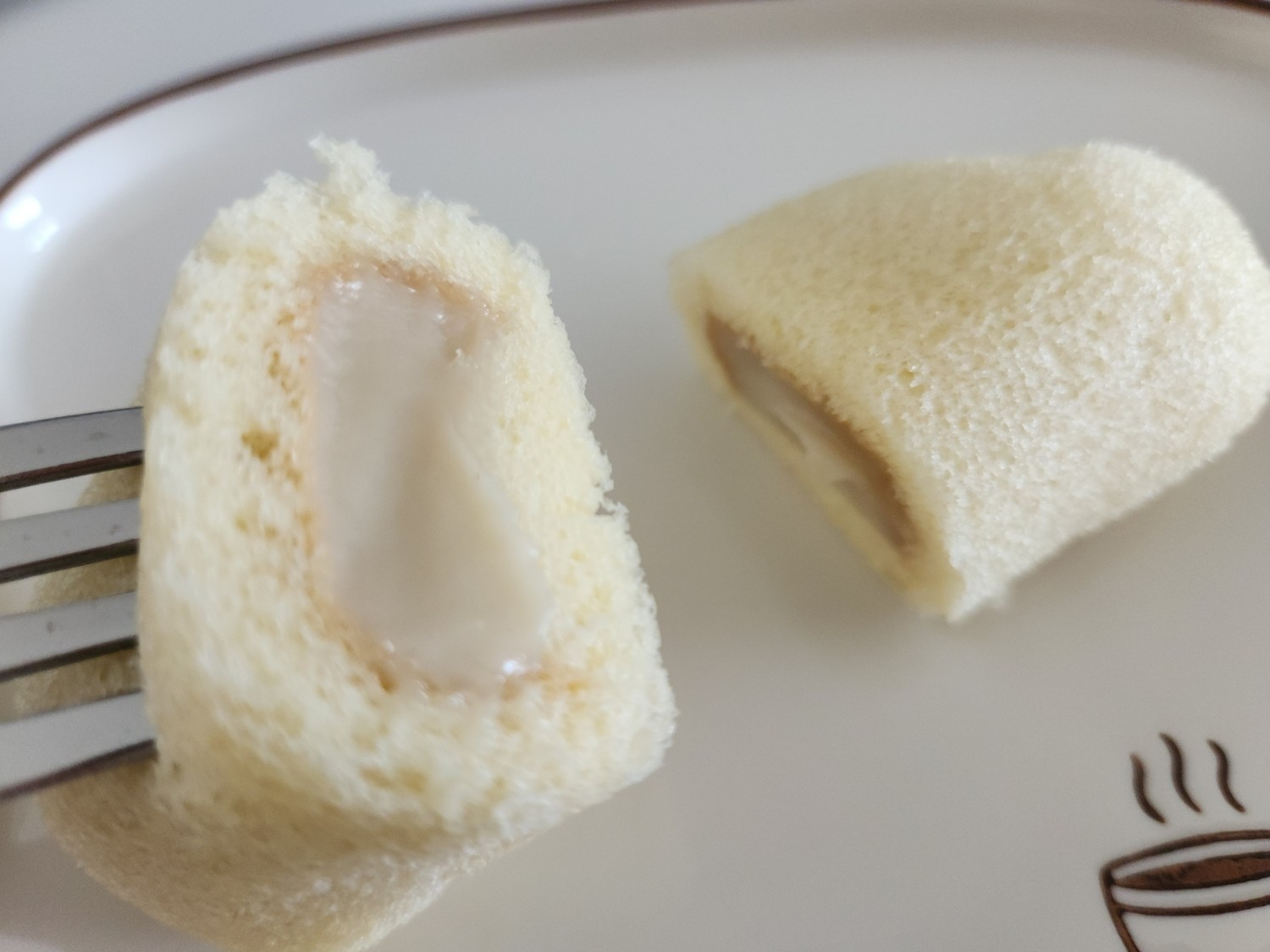 작은 빵을 반으로 갈라 포크로 찍어 든 모습. 빵 안에 바나나 커스터드 크림이 가득 차 있다