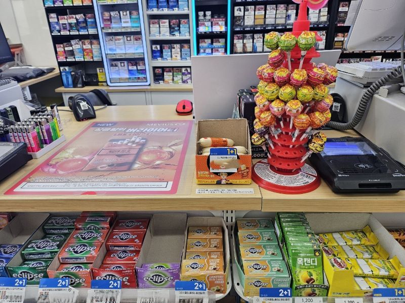 카페나 편의점 포스기 바로 옆에 진열된 사탕, 껌, 쿠키 등 저단가 상품들의 모습. 결제 대기 중인 고객의 시선이 머무는 골든 존에 충동구매를 유도하는 상품을 배치한 매장 전략 예시.