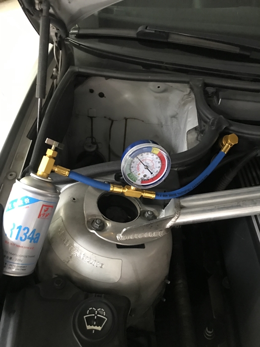 자동차 엔진룸에서 냉매 캔&amp;#44; 압력 게이지&amp;#44; 연결 호스가 모두 설치된 상태 &ndash; R134a 냉매 충전 작업 중 전체 구성