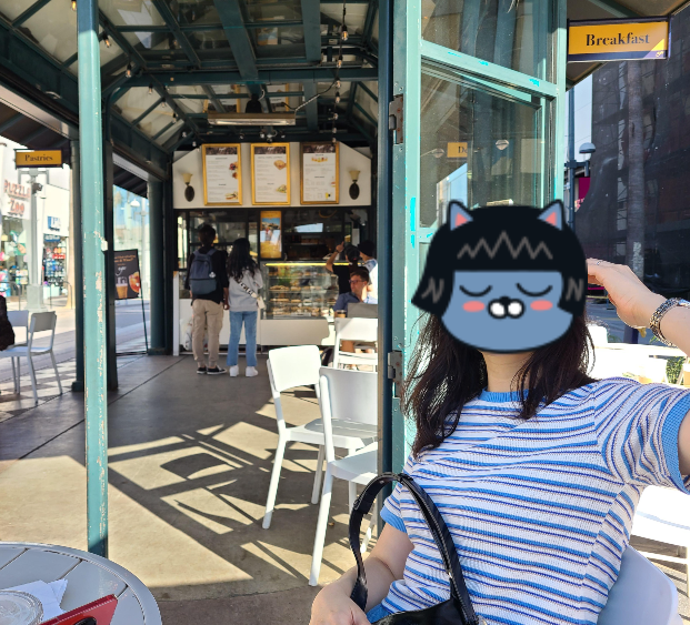 카페에 앉아 사진을 찍었다. 사방이 뻥 뚫린 야외 카페이며, 뒤로는 주문 받는 곳이 보이고 양 옆으로는 도로와 상점들이 있다.