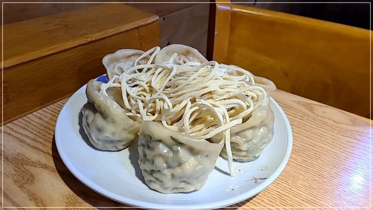 흰접시에 담긴 만두 6개 칼국수사리가 나무테이블 위에 놓여있음