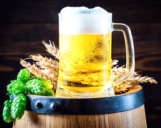 커다란 맥주통 위에 올려진 500CC 맥주컵이 있다. 컵 안에는 거품이 있는 맥주가 가득 담겨있고, 컵 뒤에는 보리들이 있다.