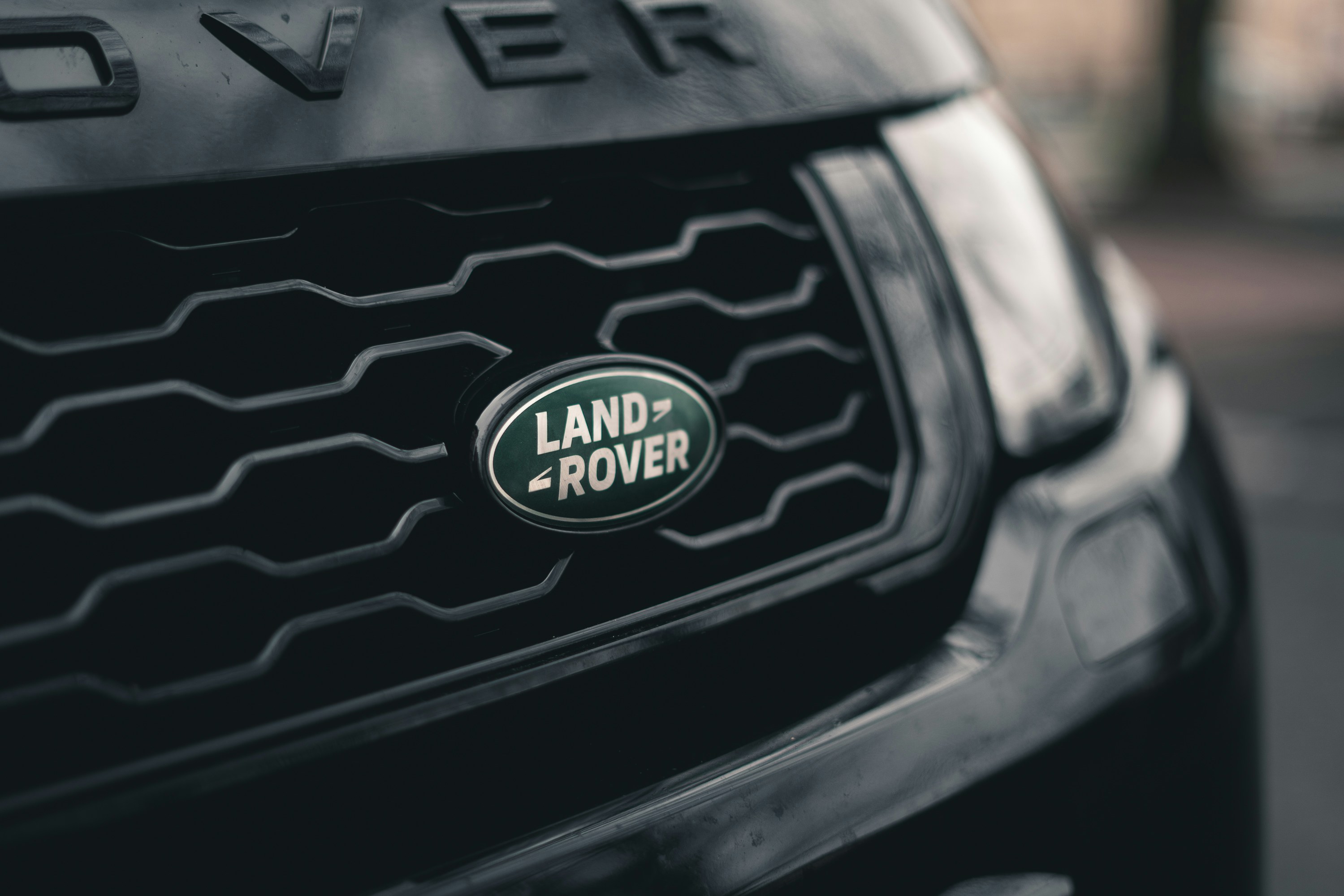어둡고 질감 있는 검은색 자동차 그릴 중앙에 녹색 타원형 랜드로버(LAND ROVER) 로고가 선명하게 보이는 클로즈업 사진