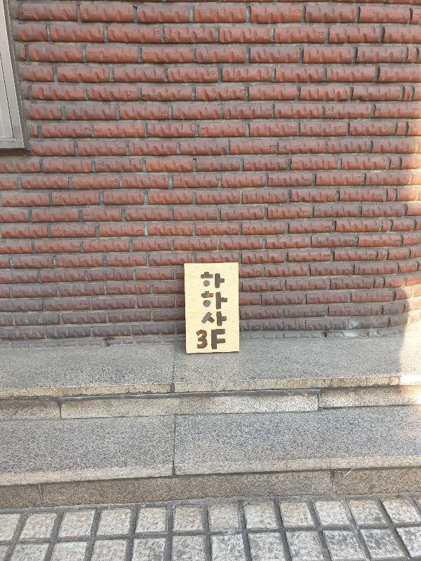 적색 벽돌 건물 벽에 기대어 놓은 작은 하하사 간판