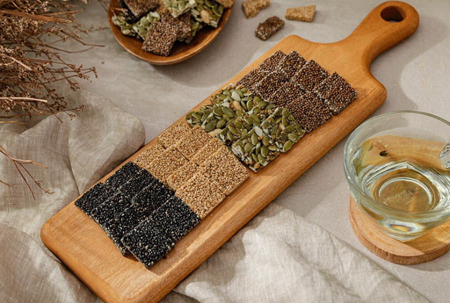 야생에서 채취를 한 검은깨와 참깨, 해바라기씨 등을 깨끗하게 세척을 한 후에 꿀과 함께 버무려서 만든 각종 강정을 나무 깔판과 그릇에 각각 가지런히 놓아두고 꿀을 담은 투명한 그릇을 옆에 두고 찍은 사진