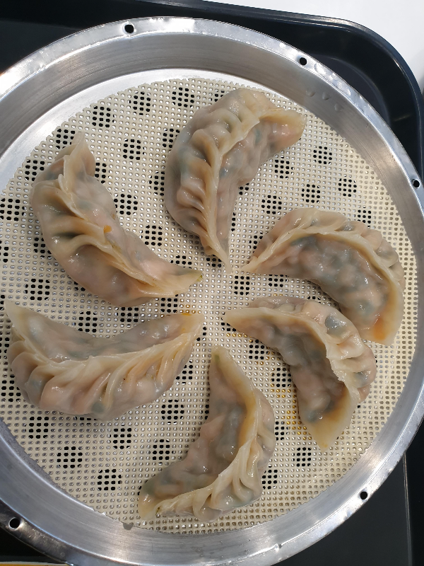 찜기 위에 놓인 6개의 만두. 내부 붉은 빛과 초록색이 비친다.