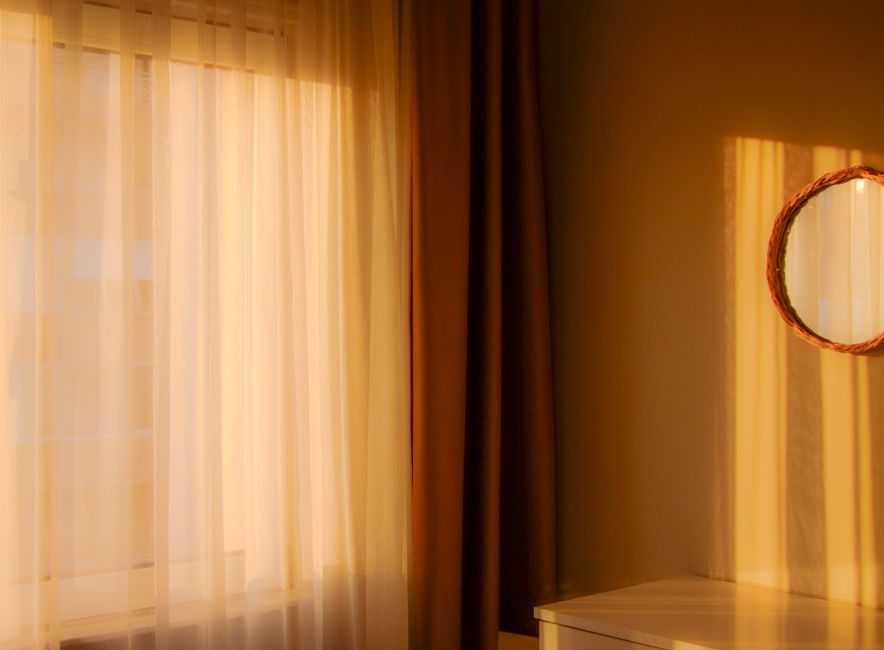 Sunlight casting warm shades through sheer curtains onto a wall and a mirror.