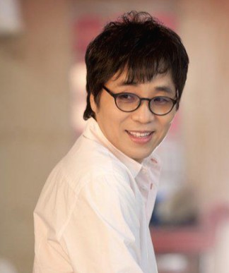 가수-이용이-트레이드-마크인-안경을-끼고-고개를-뒤로-돌려-옅은-미소를-짓고-있는-사진