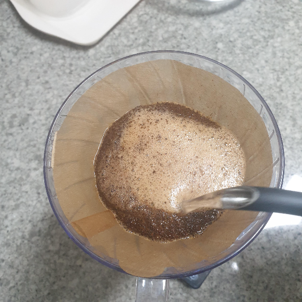 드리퍼 안에 원두가 담겨있고 드립포트로 물을 붓는 중. 거품이 전체적으로 나와 있다.