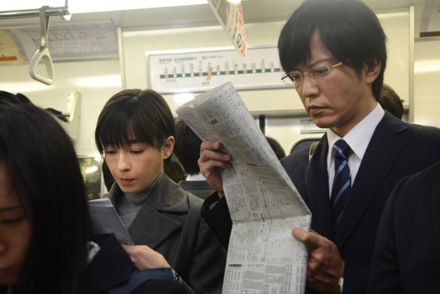 일본 영화 《종이달》의 한 장면. 평범한 일상을 살아가던 은행원이 지하철 속에서 아무렇지 않게 신문을 읽는 모습. 그러나 그 평온함 속에는 점차 무너져가는 내면과 위태로운 이중생활이 숨겨져 있다.