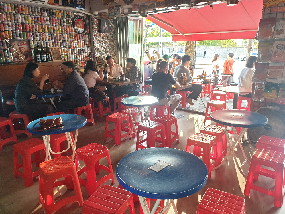 내부에는 빈 테이블이 있다. 벽면은 맥주캔으로 인테리어가 되어 있다. 테이블과 의자는 모두 플라스틱