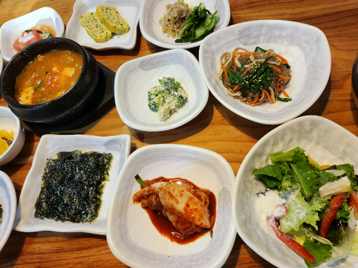 김, 김치, 잡채, 샐러드가 담긴 접시가 테이블 위에 있다