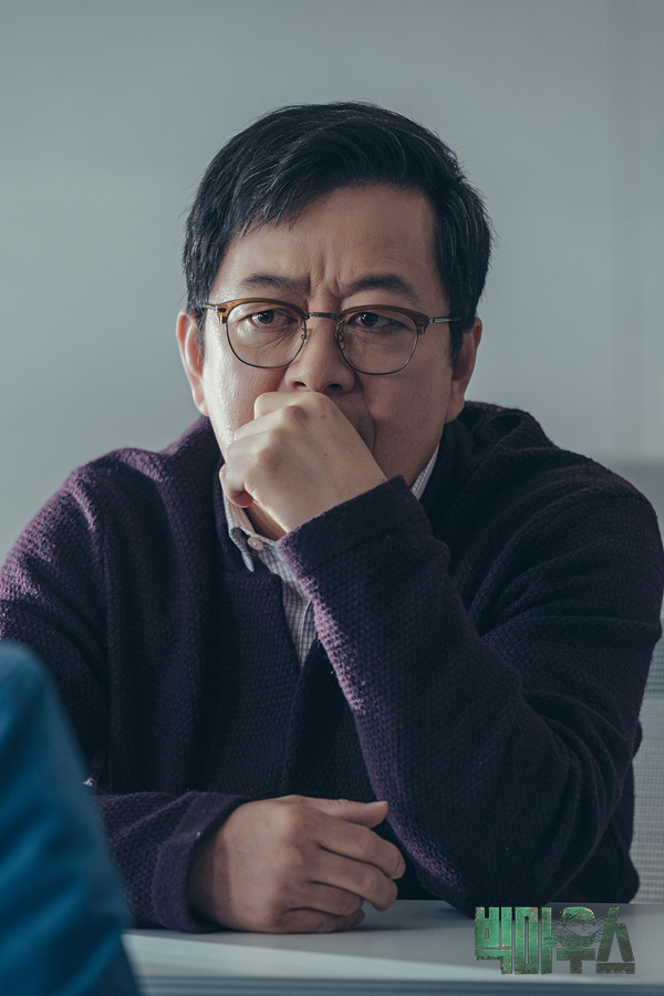 안경을 쓴 인물이 손을 입가에 대고 앉아 있는 빅마우스 현장 스틸