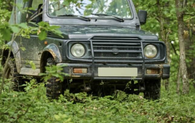 “숲속 오프로드에 주차된 중고 4륜 구동 SUV 차량, 녹색 수풀 사이에서 촬영”