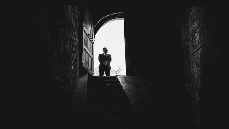 Black and white image of a man silhouetted against a bright doorway, standing on stairs.