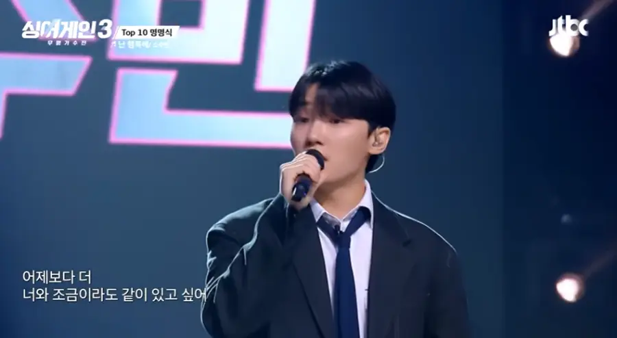 싱어게인3-
검은 무대배경 검은 양복 흰셔츠 파란넥타이 오른손에 검은마이크를 잡고 노래하는 소수빈