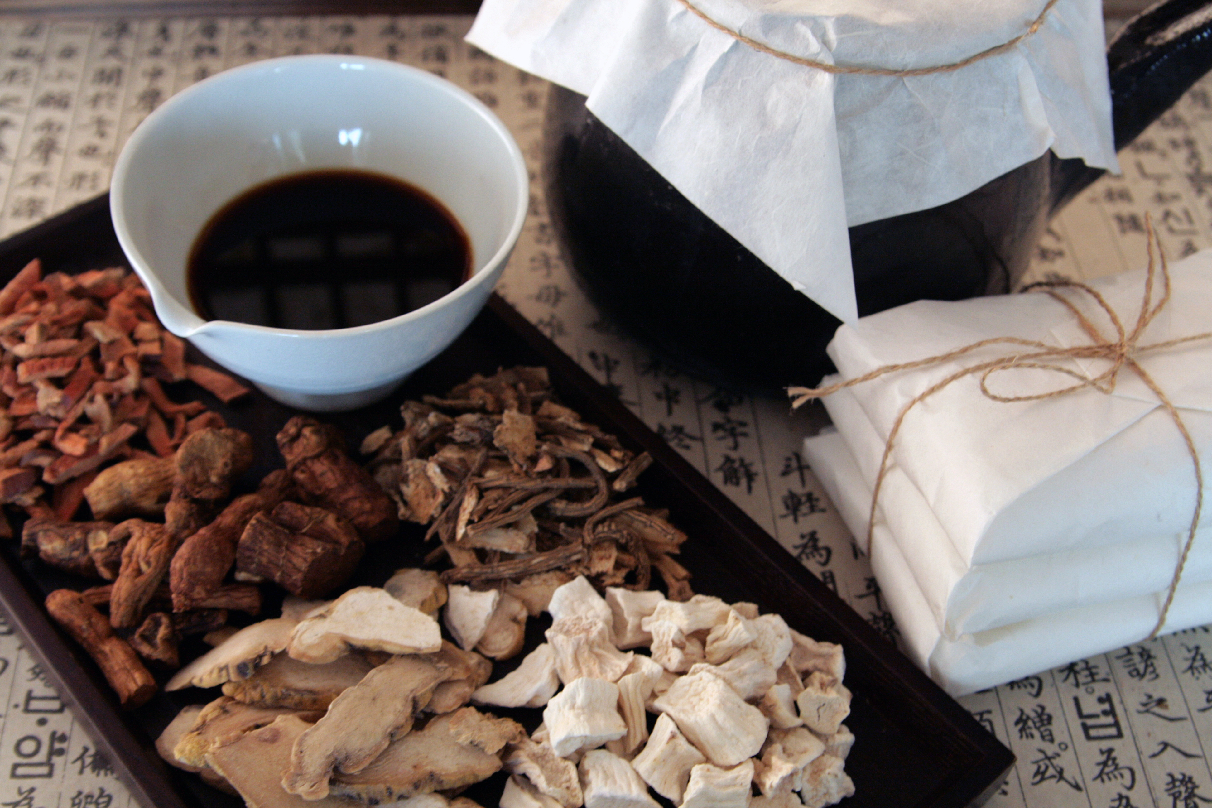 한문이 적혀 있는 종이 바닥 위에 네모난 나무 쟁반을 두고 그 위에 하얀 사기그릇에 한약을 반쯤 담아 두고&#44; 그 옆에는 각종 한약재를 두었고&#44; 나무 쟁반 옆에 전통 약탕기와 종이로 한약을 쌓은 첩약을 3첩 끈으로 묶어 놓은 사진