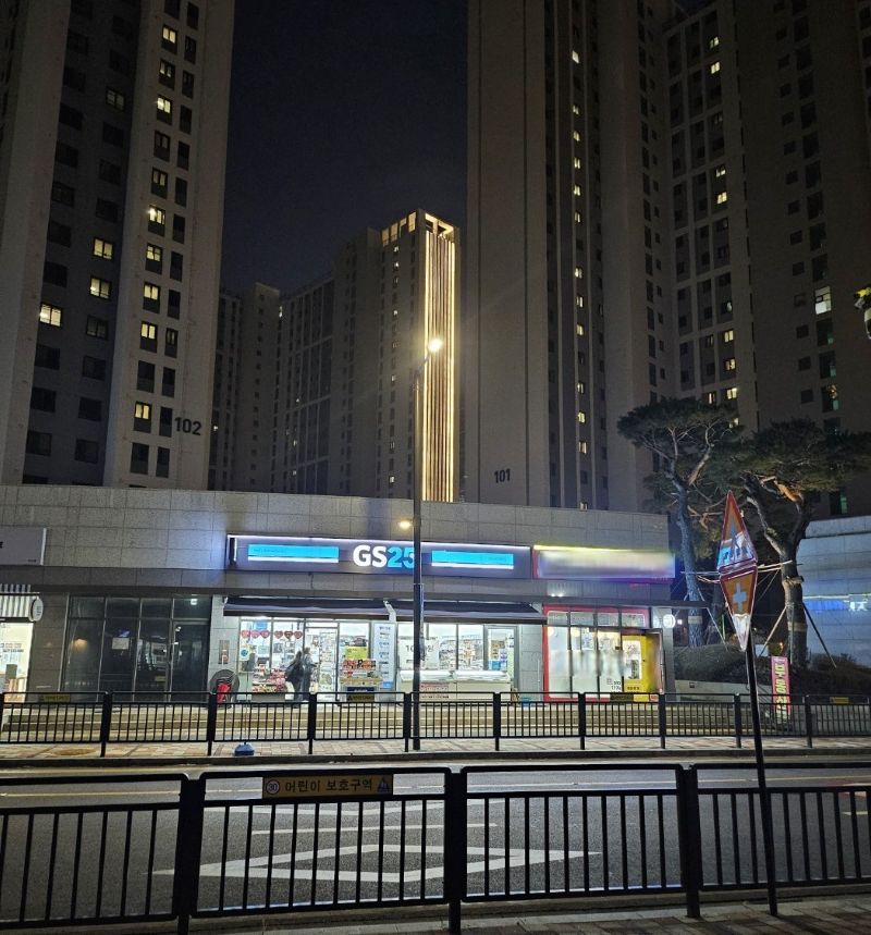 어두운 밤, 대단지 아파트 상가 1층에서 따뜻한 노란 불빛을 밝히며 이웃들을 맞이하는 동네 GS25 편의점의 밤 풍경.